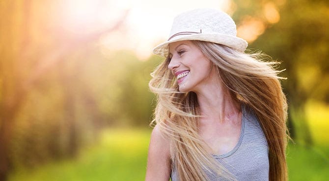 Cosmetic-Dentistry Woman with long blonde hair wearing a hat and braces smiling in sunlight