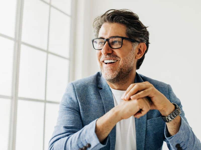 man-in-glasses-sitting-by-window-smiling-with-teeth
